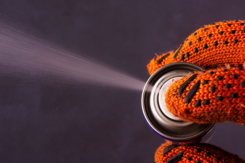 Hand mit dickem Handschuh drückt auf den Knopf einer Sprühdose und ein Sprühstoß technischen Sprays kommt vorne heraus